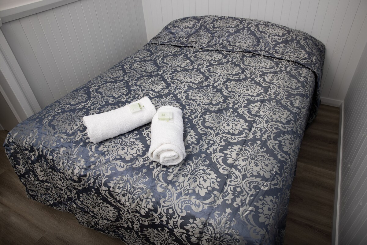A neatly made bed with a patterned bedspread and two rolled towels.