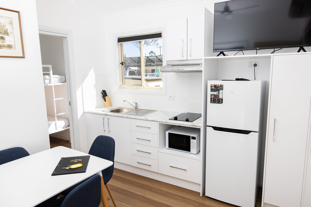 A compact kitchen with white cabinets, a microwave, a refrigerator, a sink, and a window with a view of the outside.