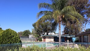 Ein Poolbereich mit einem umzäunten Pool, Palmen und einem Gebäude mit blauem Dach im Hintergrund.
