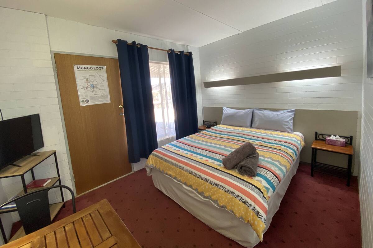 Una habitación de hotel con una cama, un escritorio, una silla, una mesita y un televisor.