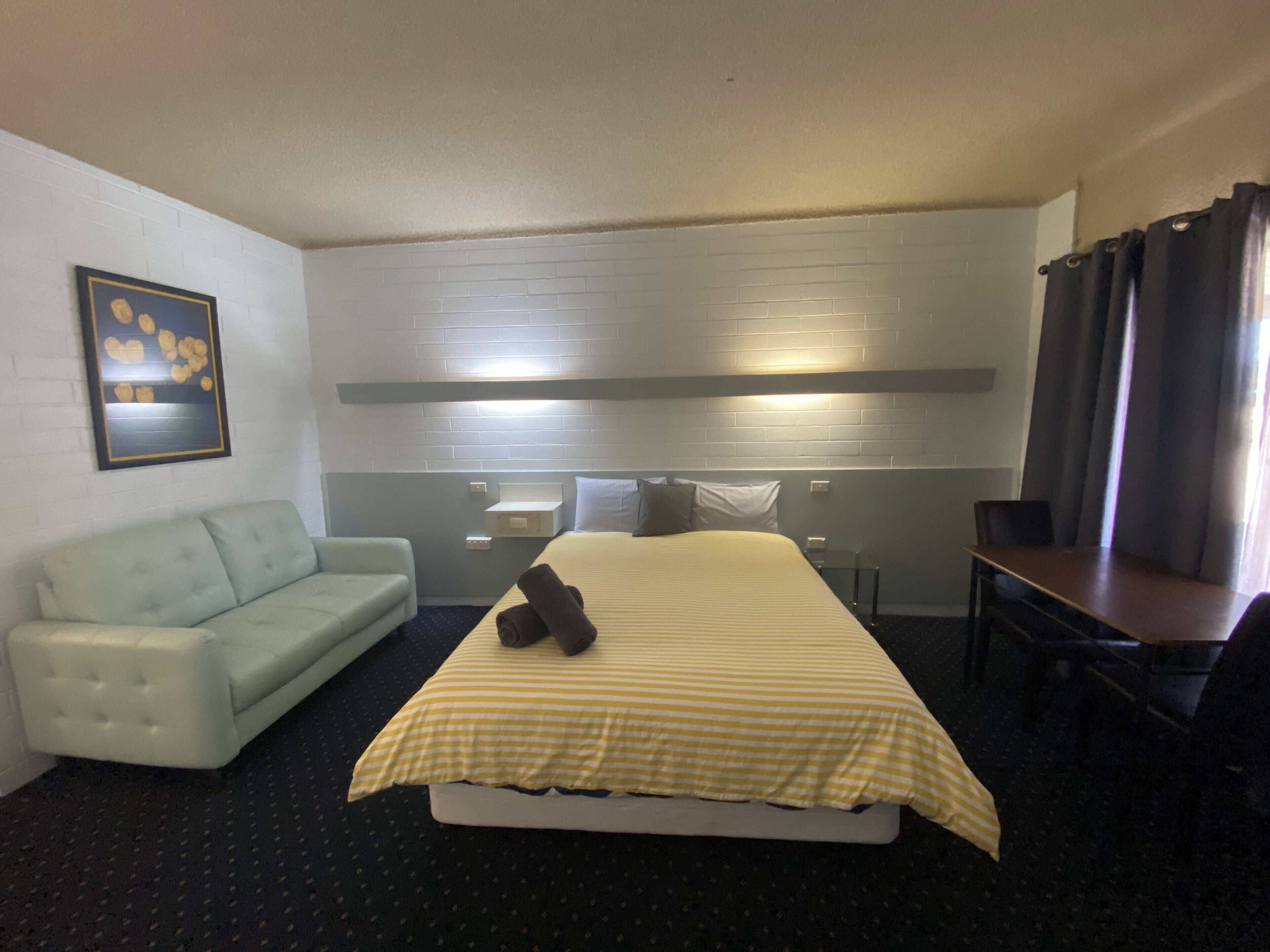 A hotel room with a bed, a sofa, a desk, and a wall-mounted shelf.