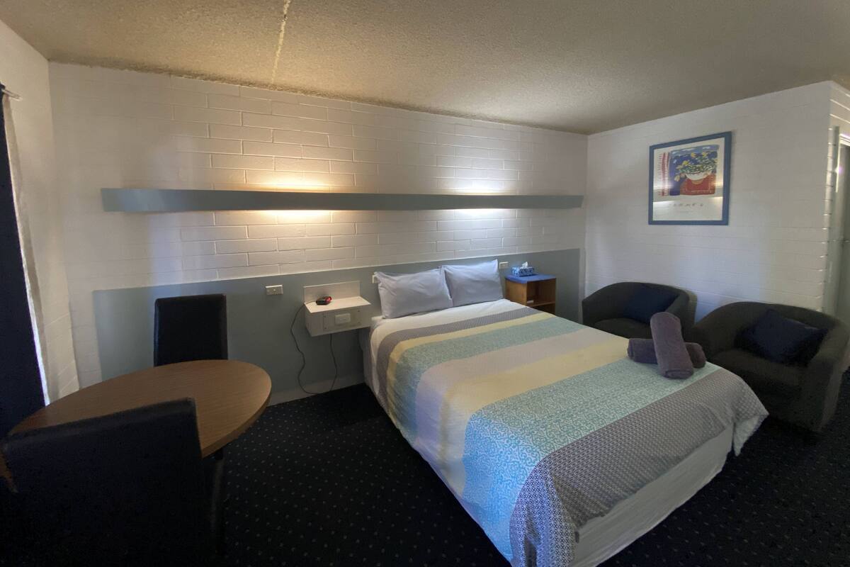 Una habitación de hotel con cama, escritorio, silla y mesita de noche.