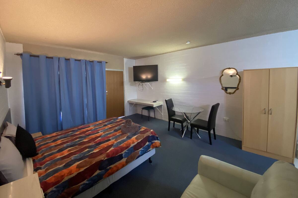 Habitación de hotel con cama, escritorio, silla, televisor y armario.