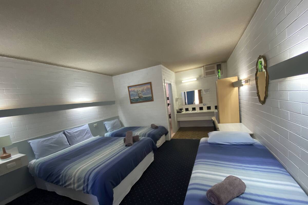 Habitación de hotel con dos camas, un baño pequeño y un espejo.