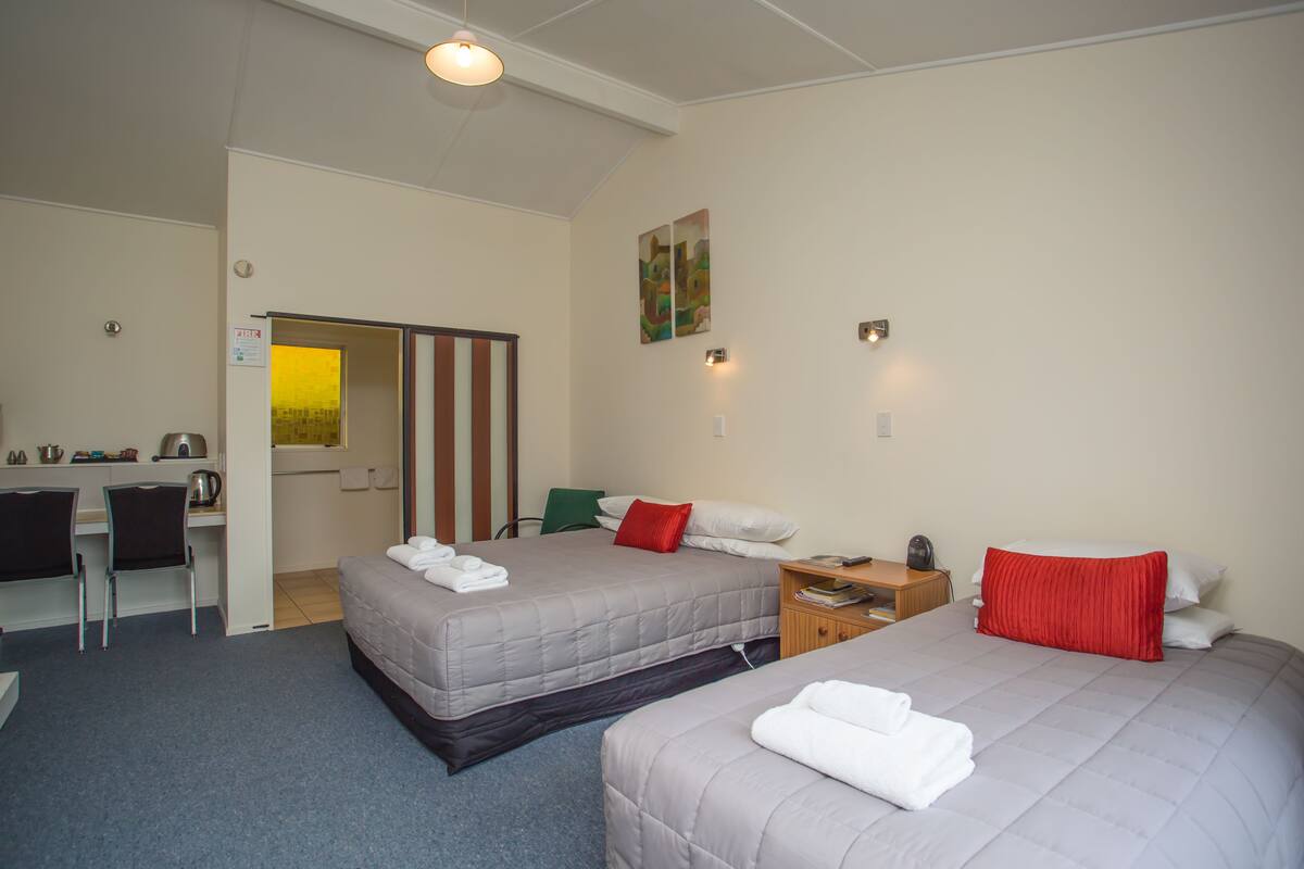 A hotel room with two beds, a desk, chairs, and a small kitchenette.