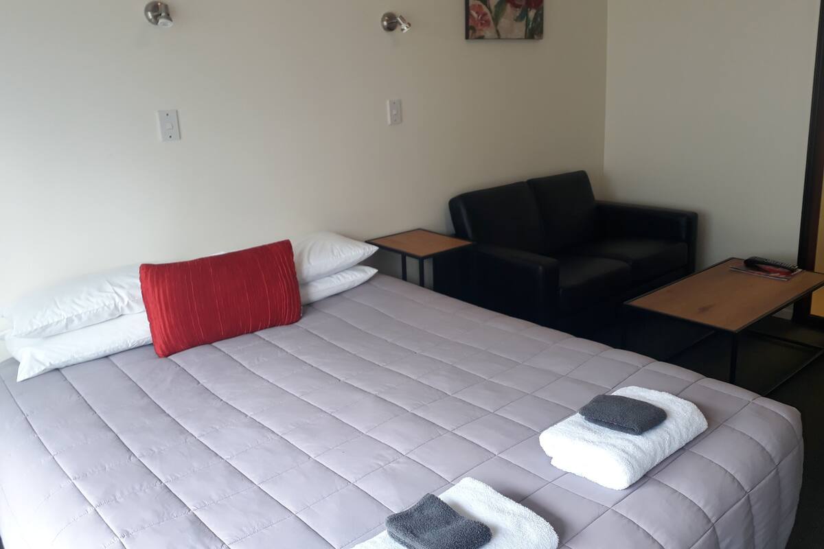 A hotel room with a bed, a chair, a table, and a painting on the wall.