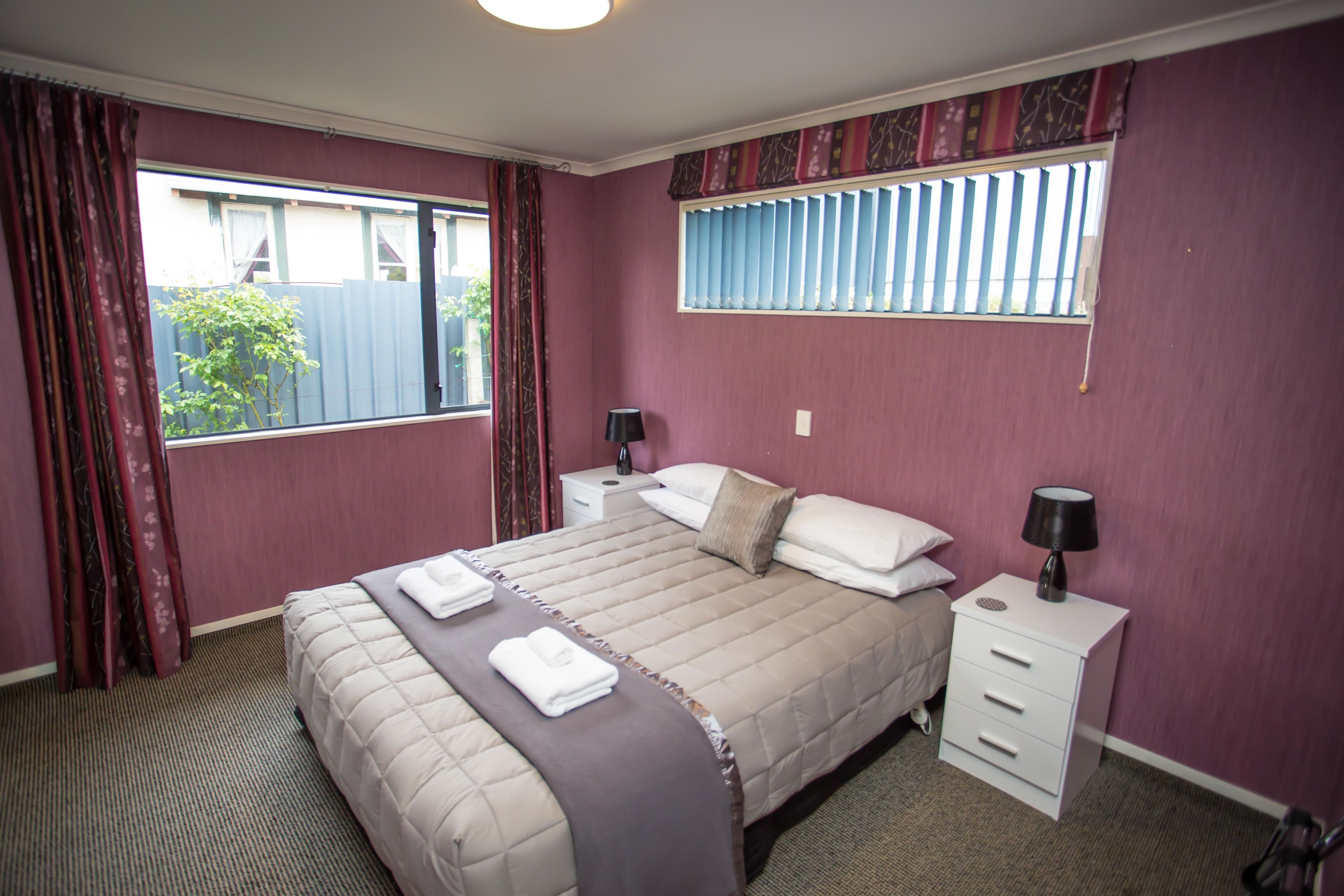 Un dormitorio con cama, dos mesitas de noche, una ventana con cortinas y vistas al exterior.