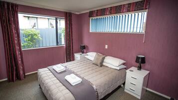 Un dormitorio con cama, dos mesitas de noche, una ventana con cortinas y vistas al exterior.