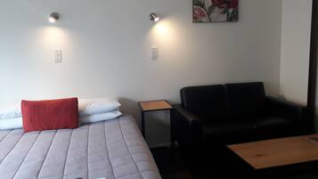 Una habitació amb un llit, un sofà de pell negra, una taula de fusta petita i un quadre a la paret.