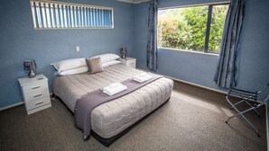 Ein Schlafzimmer mit Bett, Nachttischen, einem Fenster mit Vorhängen und Blick ins Grüne.