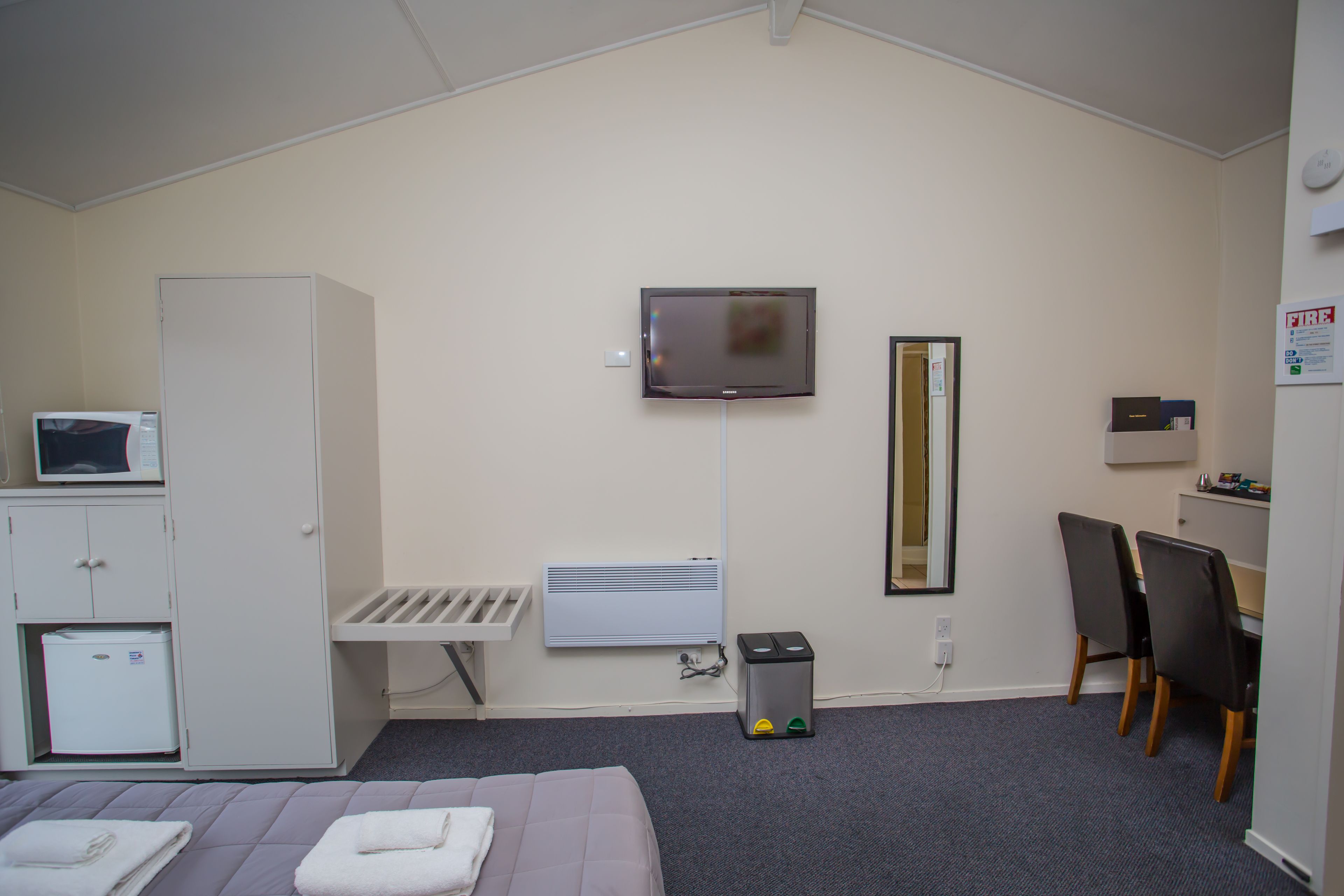 Habitación de hotel con cama, escritorio, televisor, espejo, microondas, mini refrigerador y un cesto de basura.