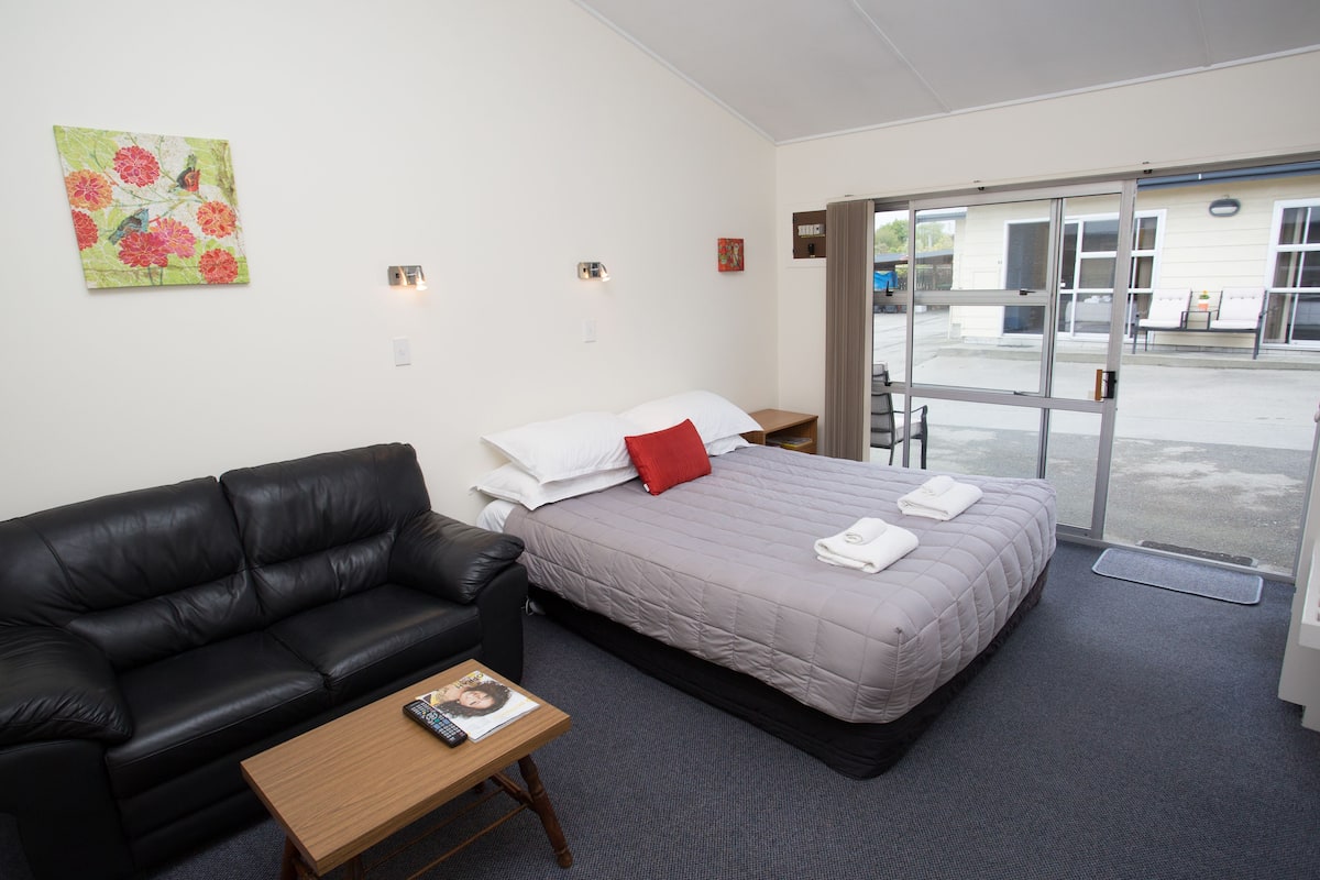 A hotel room with a bed, a black leather sofa, a small wooden table, and a painting on the wall.