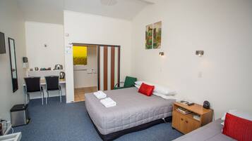 A hotel room with a bed, a desk, two chairs, a small cabinet, and a door leading to another room.