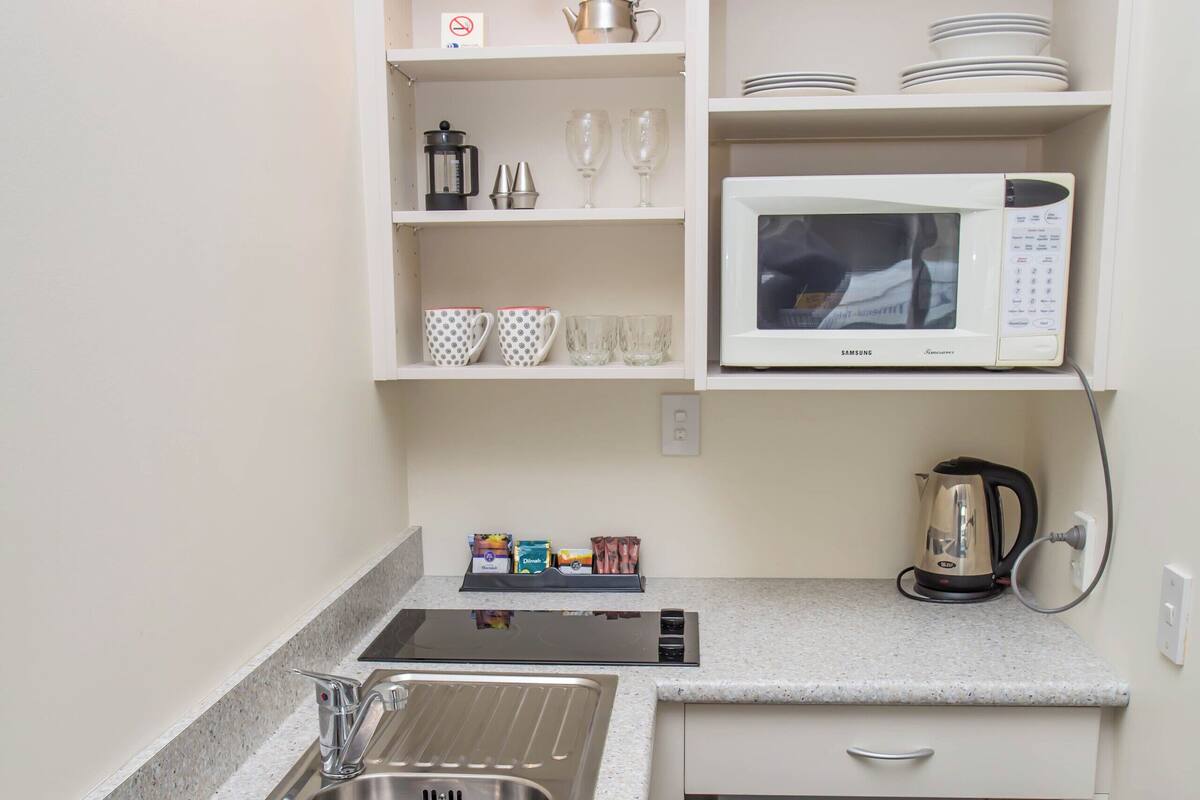 A compact kitchen with a stainless steel sink, a microwave, a kettle, and a small refrigerator.