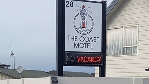 Ein Schild eines Motels mit dem Leuchtturm-Logo, das anzeigt, dass es sich um The Coast Motel handelt, und eine digitale Anzeige mit der Meldung 'Keine Zimmer frei'.