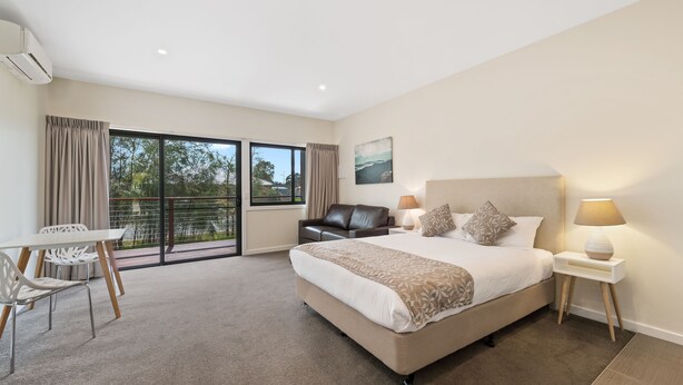 A modern hotel room with a large bed, a desk, and a view of the outdoors through a sliding door. - High Country Holiday Park (Mansfield)