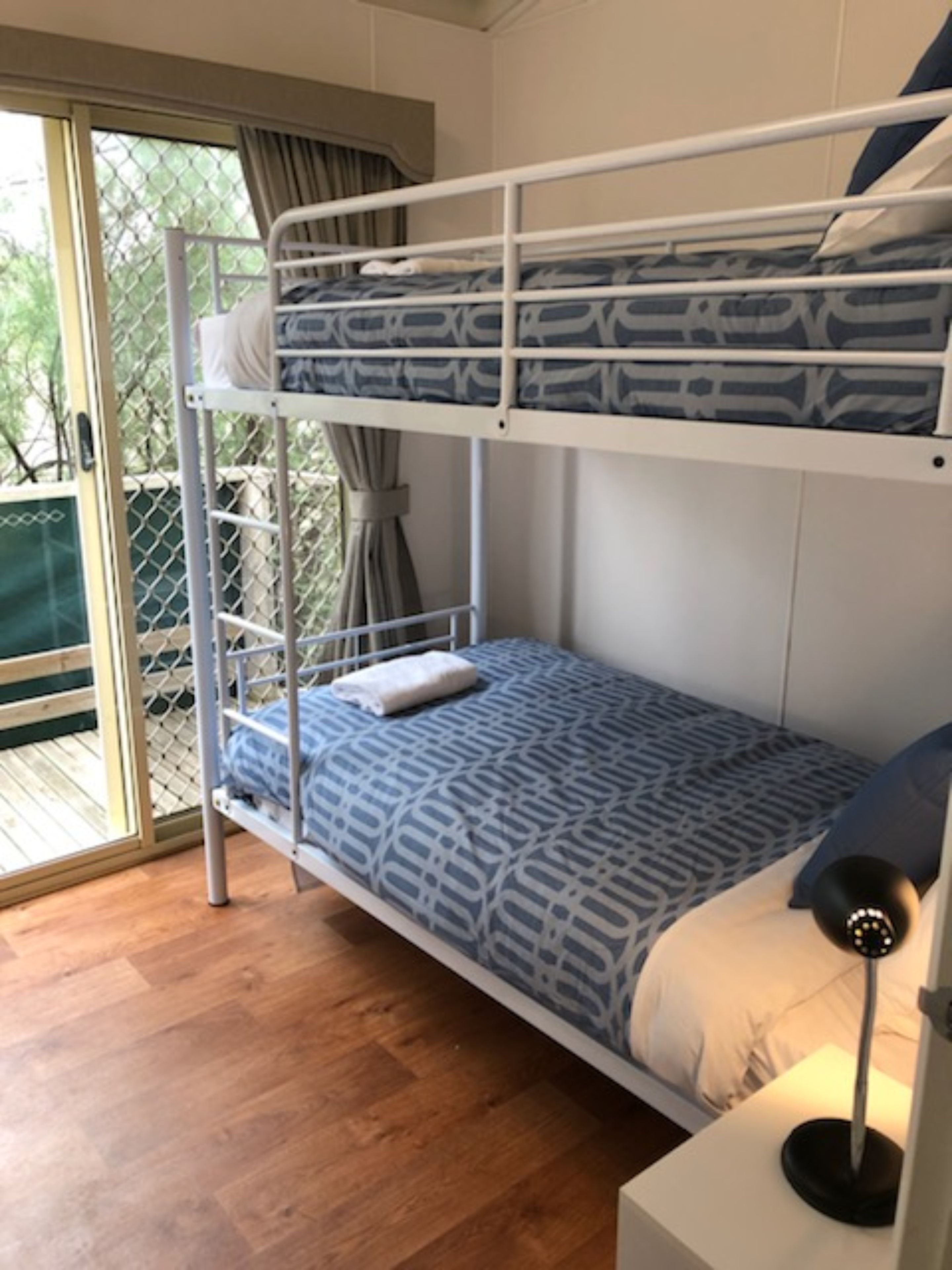 A bunk bed with a patterned bedspread, a bedside lamp, and a view through a glass door.