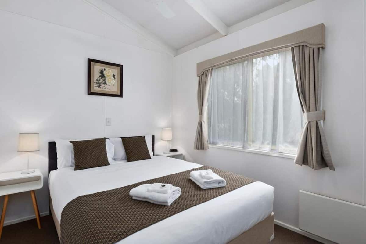 A hotel room with a large bed, two bedside tables, a window with curtains, and a framed picture on the wall.