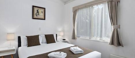 Een hotelkamer met een groot bed, twee nachtkastjes, een raam met gordijnen en een ingelijste foto aan de muur.