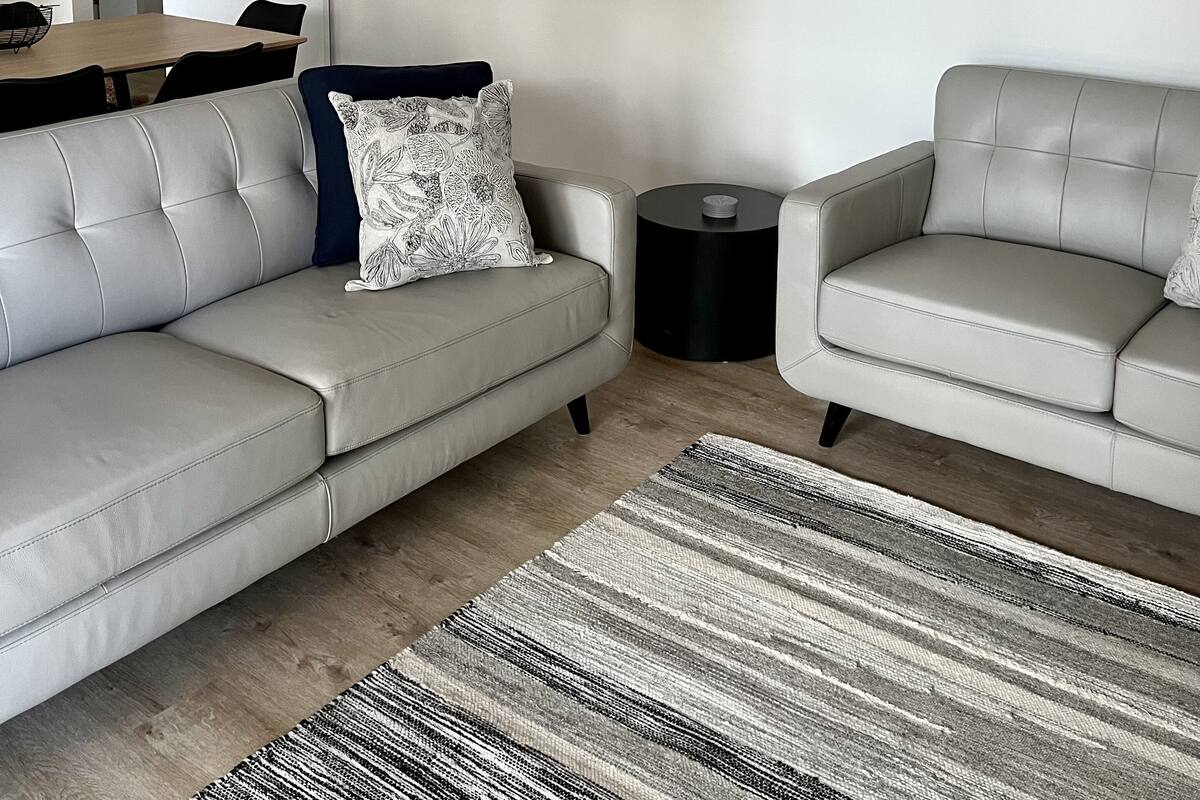 A modern living room with a sofa, two armchairs, a coffee table, a side table, and a painting on the wall.