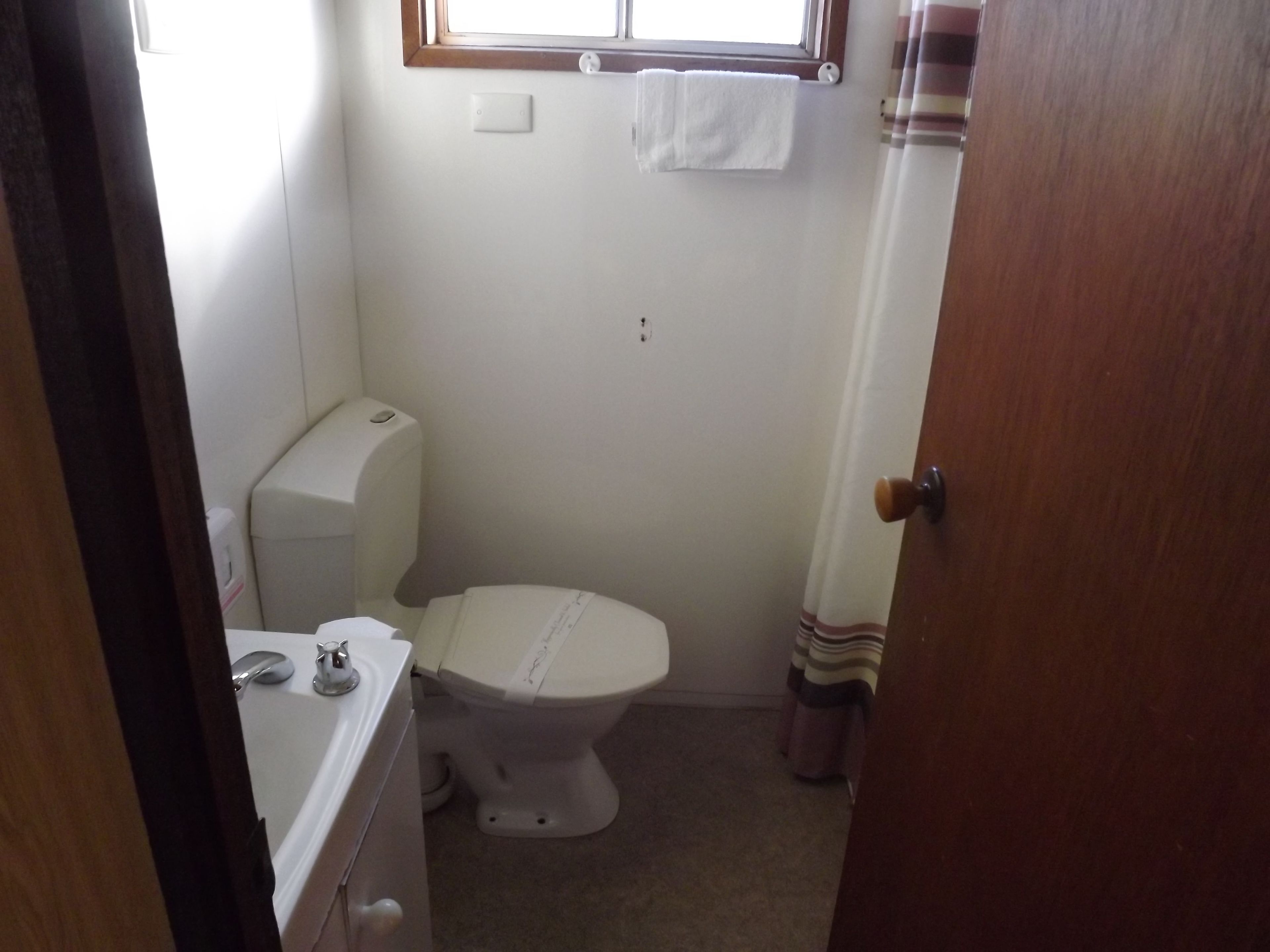 Ein kleines, kompaktes Badezimmer mit Toilette, Waschbecken und einem Fenster über der Toilette.