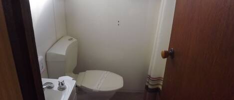 Ein kleines, kompaktes Badezimmer mit Toilette, Waschbecken und einem Fenster über der Toilette.