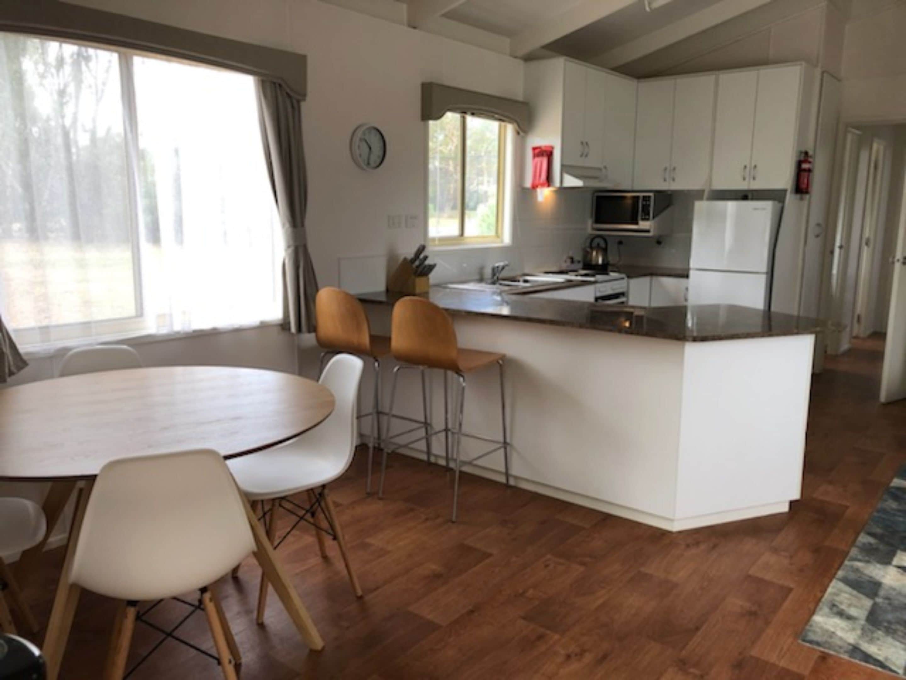 Una cocina moderna con armarios blancos, una isla central y un comedor con una mesa redonda y dos sillas.