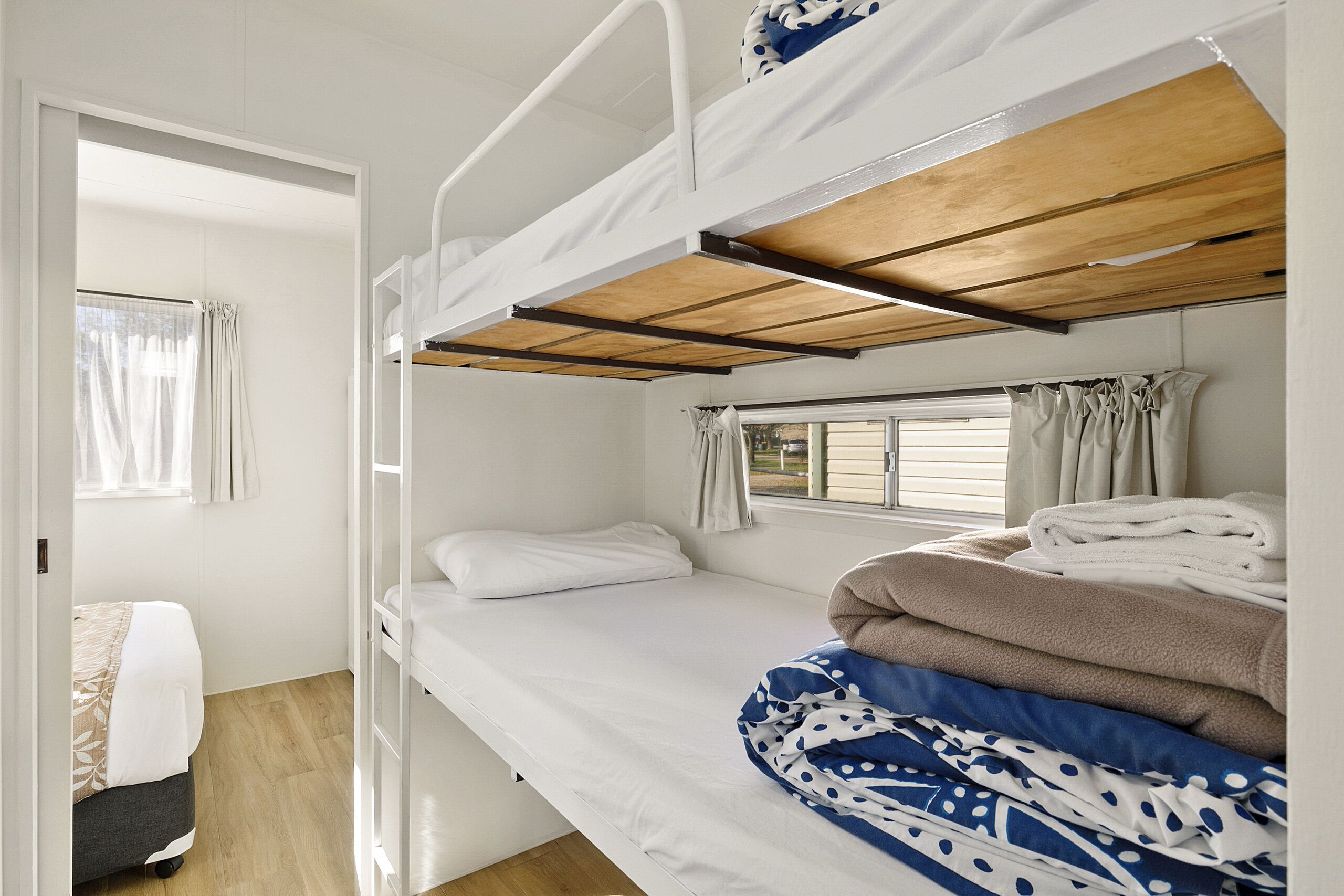 A bunk bed room with a window, a door, and a small bedside table.