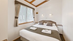 A hotel room with a large bed, a ceiling fan, a window with curtains, and a nightstand with a lamp. - High Country Holiday Park (Mansfield)