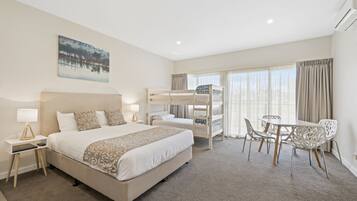 A hotel room with a large bed, a bunk bed, a dining area with chairs, and a painting on the wall.
