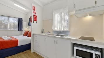 A modern hotel room with a bed, a kitchenette, a window with curtains, and a fire extinguisher on the wall.