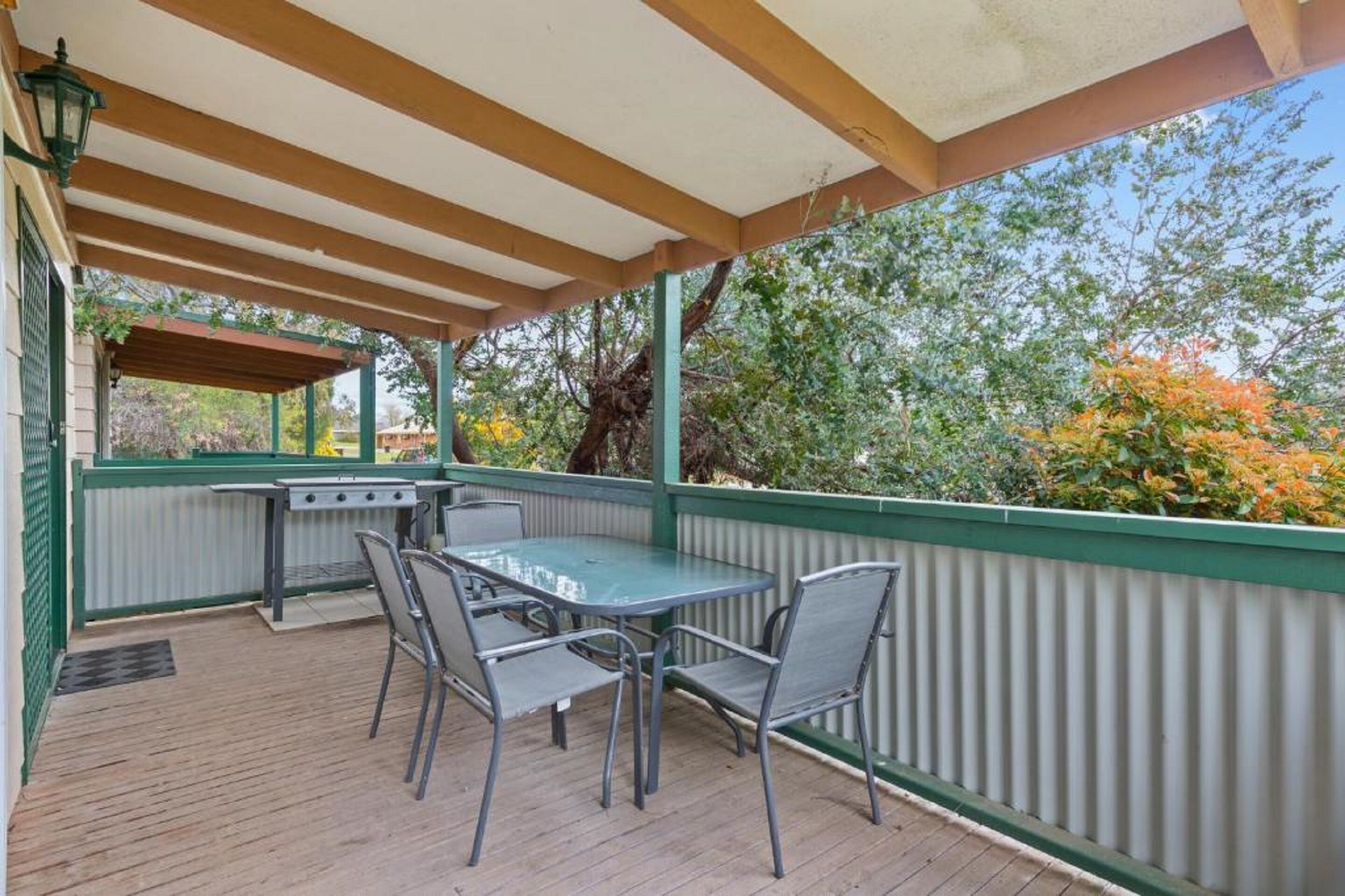 An outdoor patio with a table and chairs, a grill, and a view of trees and foliage.