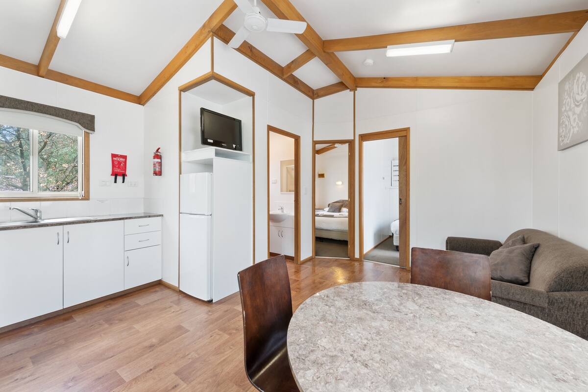 A modern kitchen with white cabinets, a built-in TV, and a dining area with a marble table and chairs.