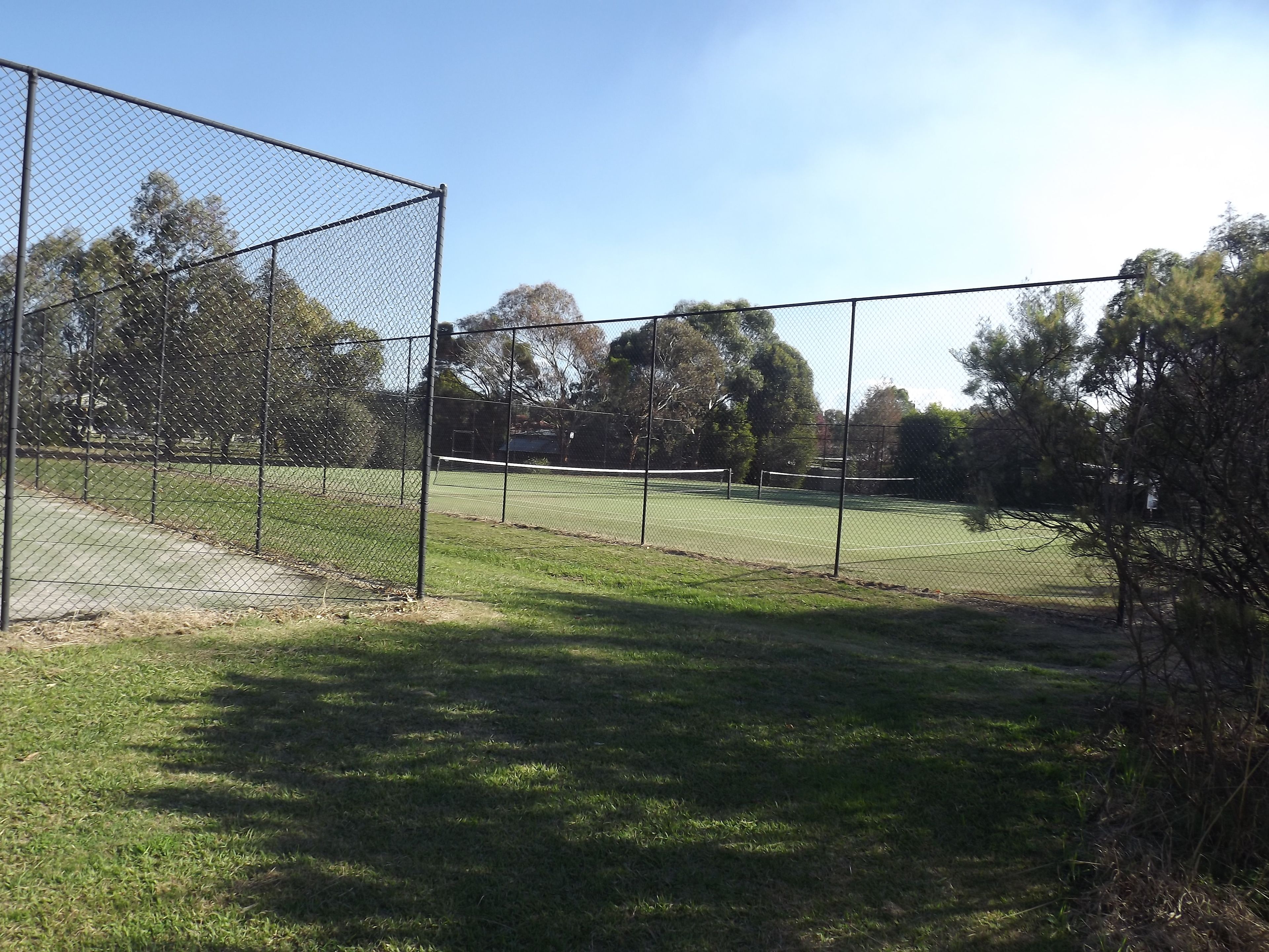 A fenced tennis court with a net in the middle, surrounded by trees and a clear sky.