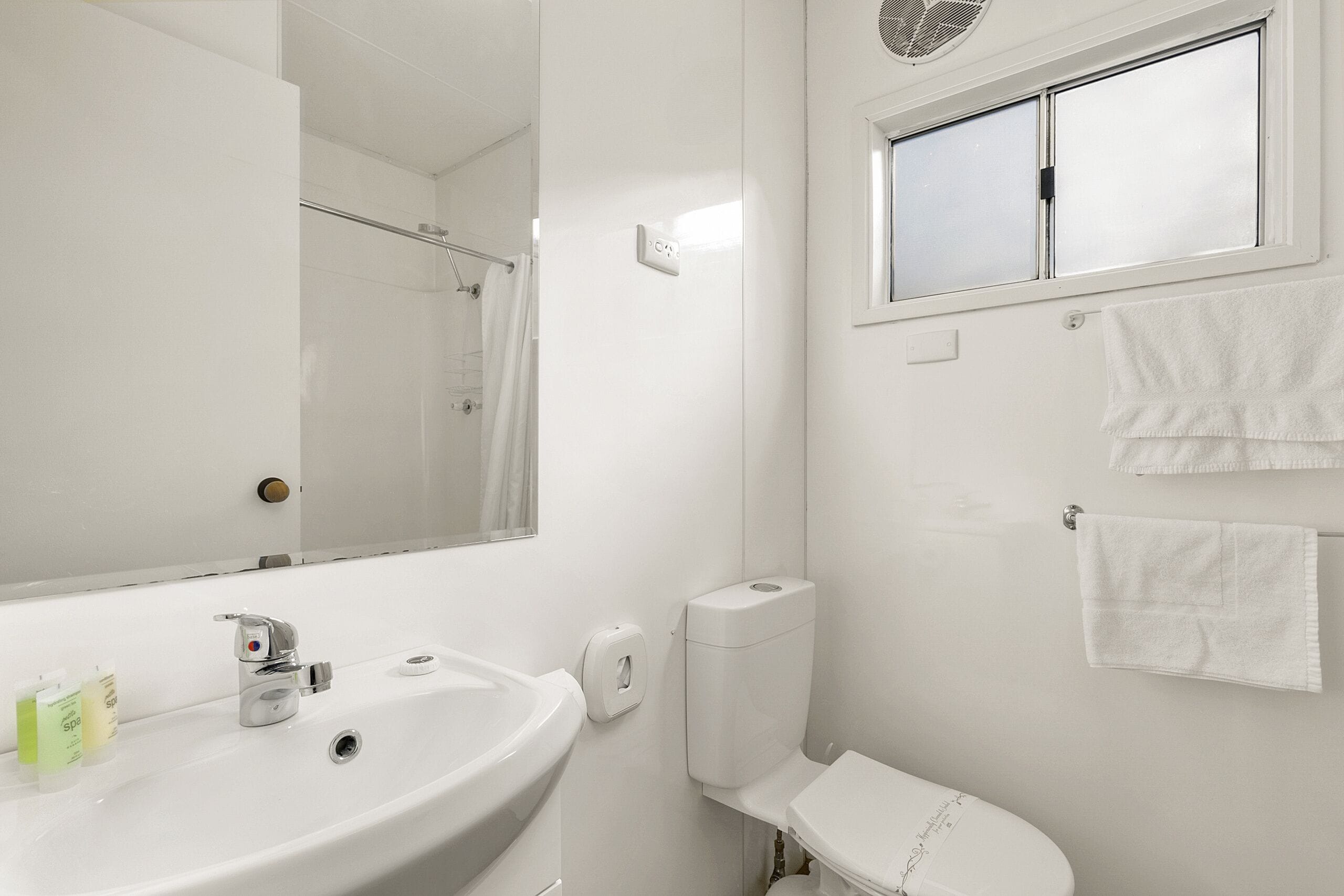 Ein Badezimmer mit Waschbecken, Spiegel, Toilette und Fenster.