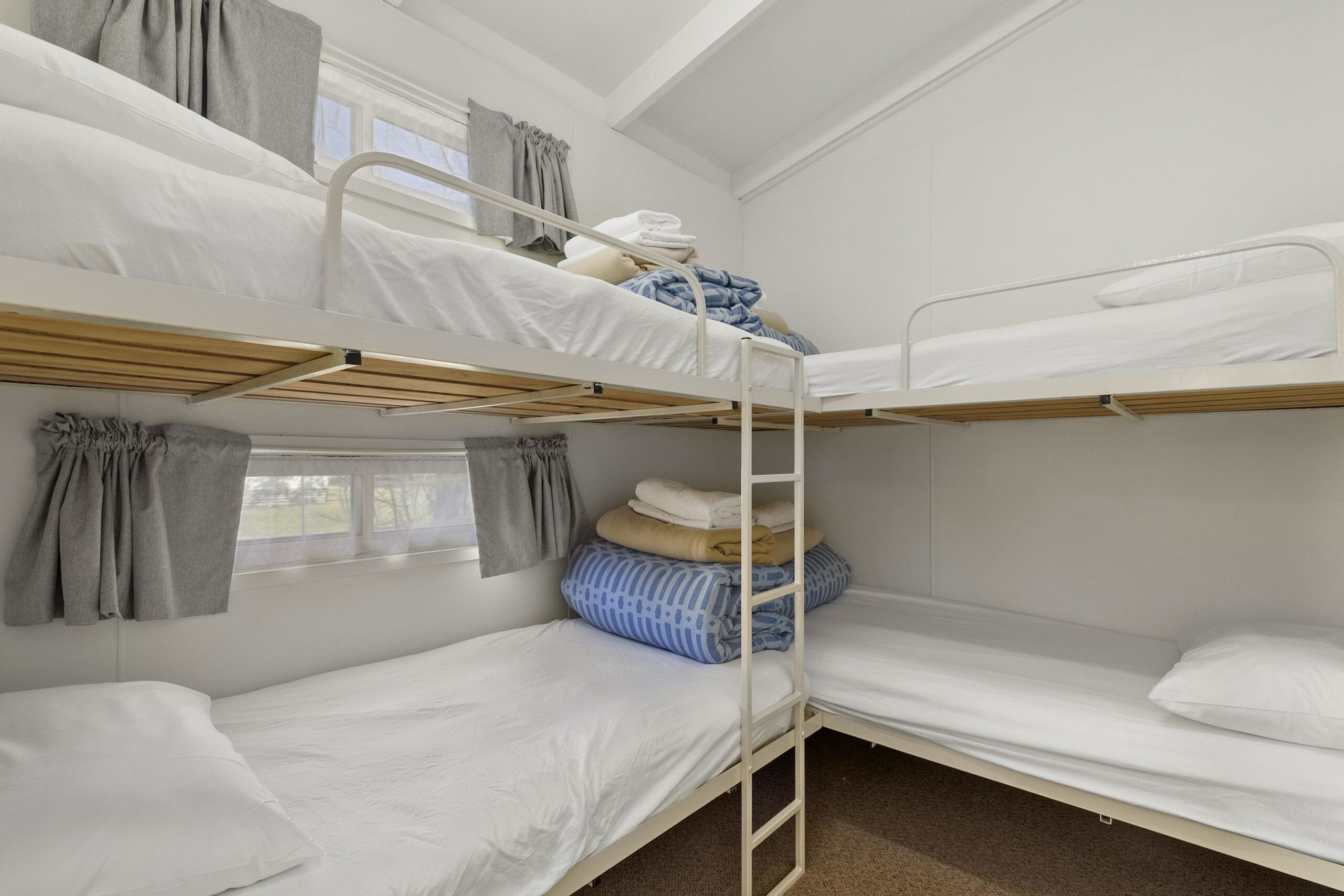 Une chambre avec un lit superposé, du linge de lit blanc, une fenêtre avec des rideaux et une échelle.