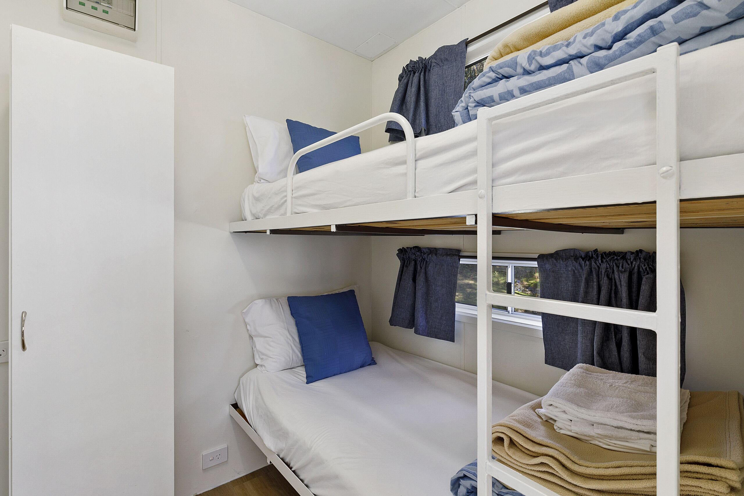 A bunk bed room with white bedding, a door, and a window with curtains.