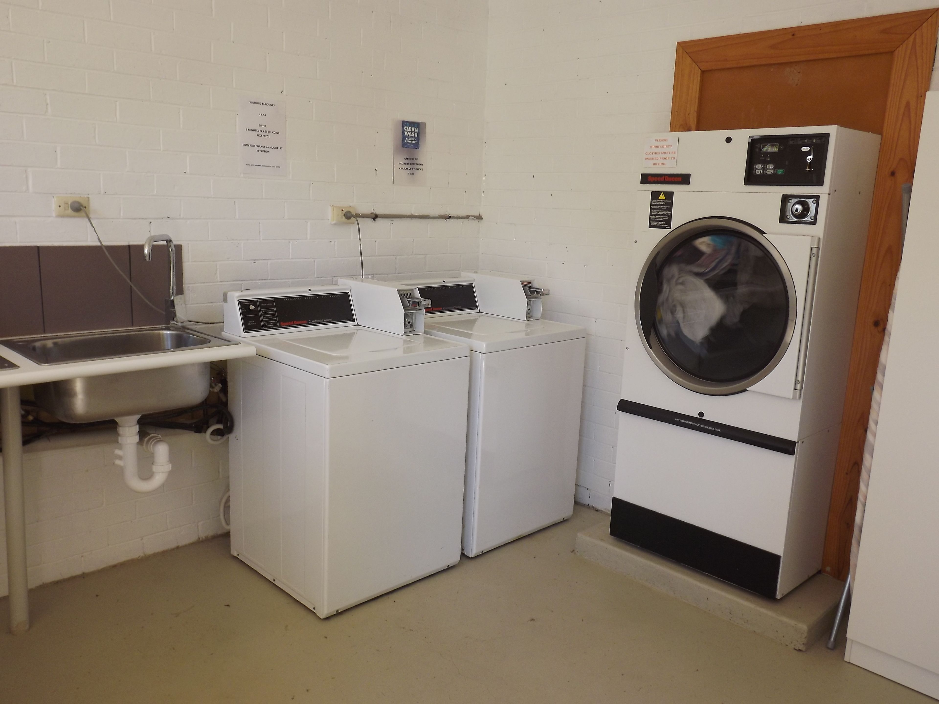 A laundry room with two front-loading washing machines, a sink, and a wooden door.