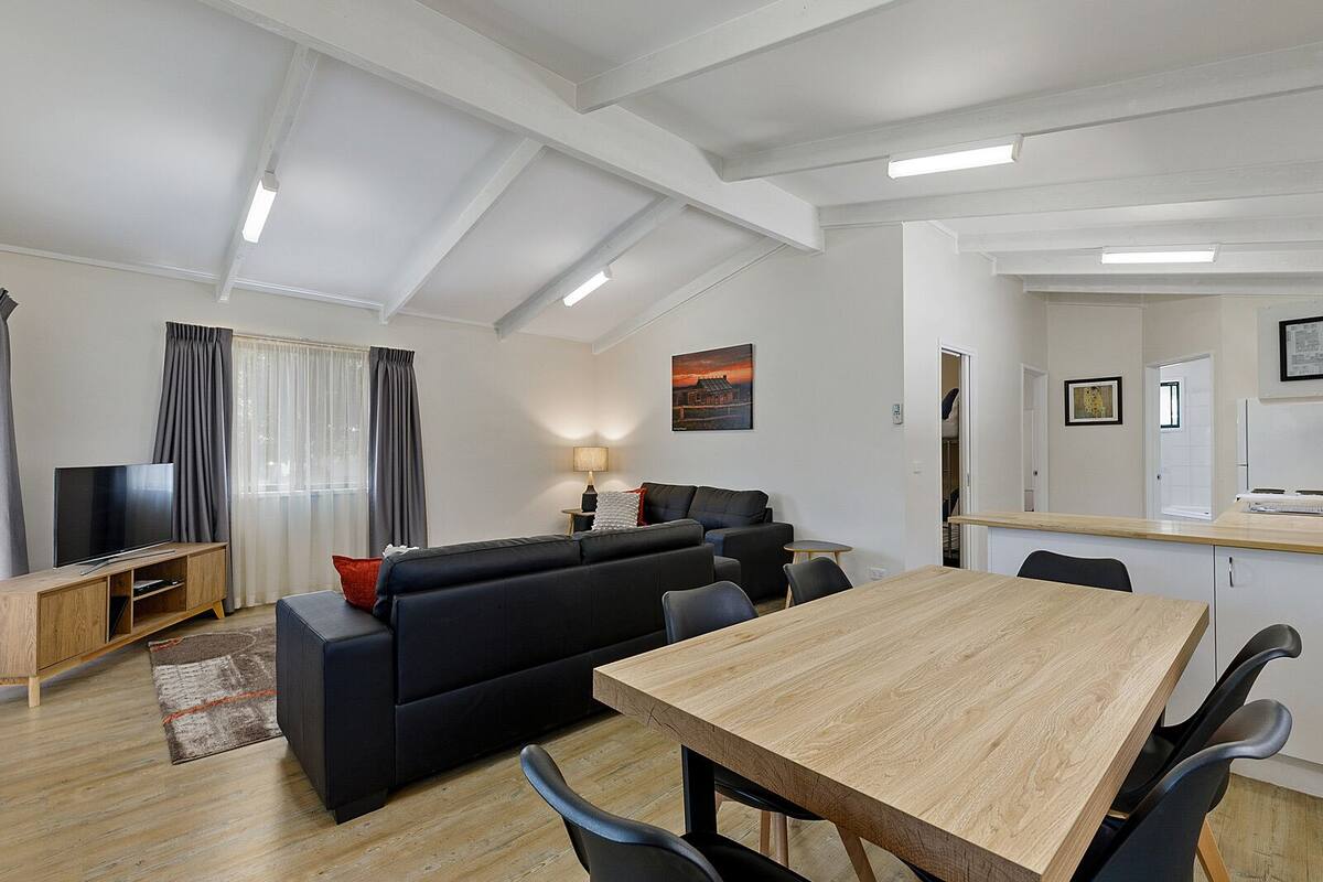 A modern living room with a sofa, TV, dining table, and kitchen area.