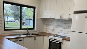 A modern kitchen with white cabinets, a wooden countertop, a built-in oven, and a refrigerator. - High Country Holiday Park (Mansfield)