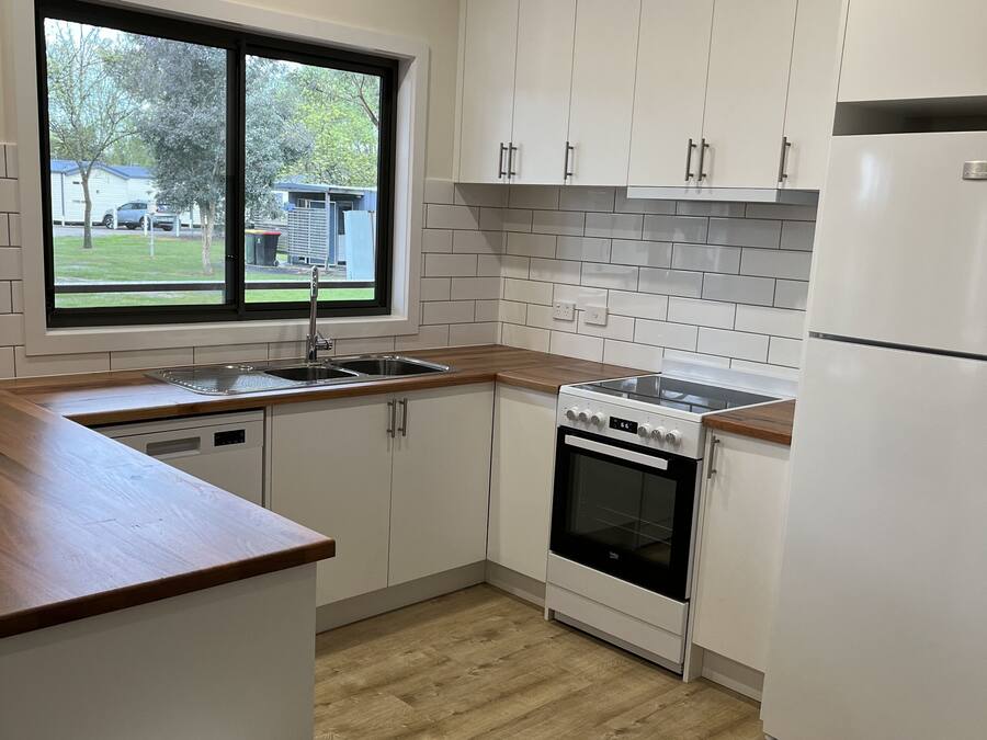 A modern kitchen with white cabinets, a wooden countertop, a built-in oven, and a refrigerator.