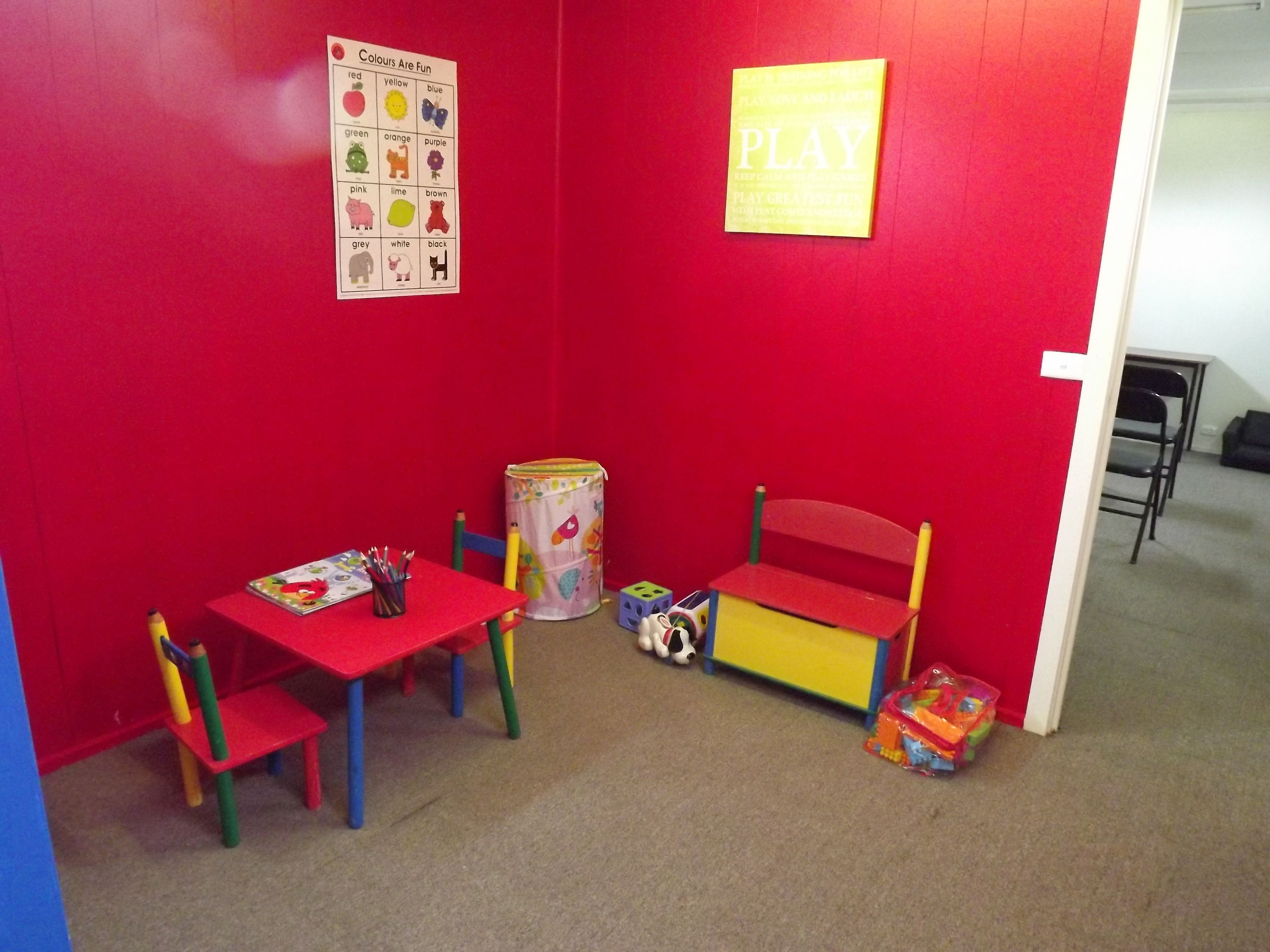 Ein Spielzimmer mit roter Wand, einer Spieledecke, einem kleinen Tisch, Stühlen und einer Spielzeugaufbewahrungsbox.