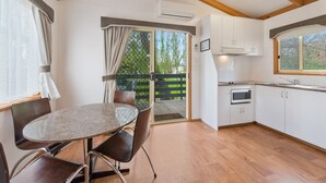 A kitchen with a dining area, wooden flooring, and a sliding glass door leading to an outdoor deck. - High Country Holiday Park (Mansfield)