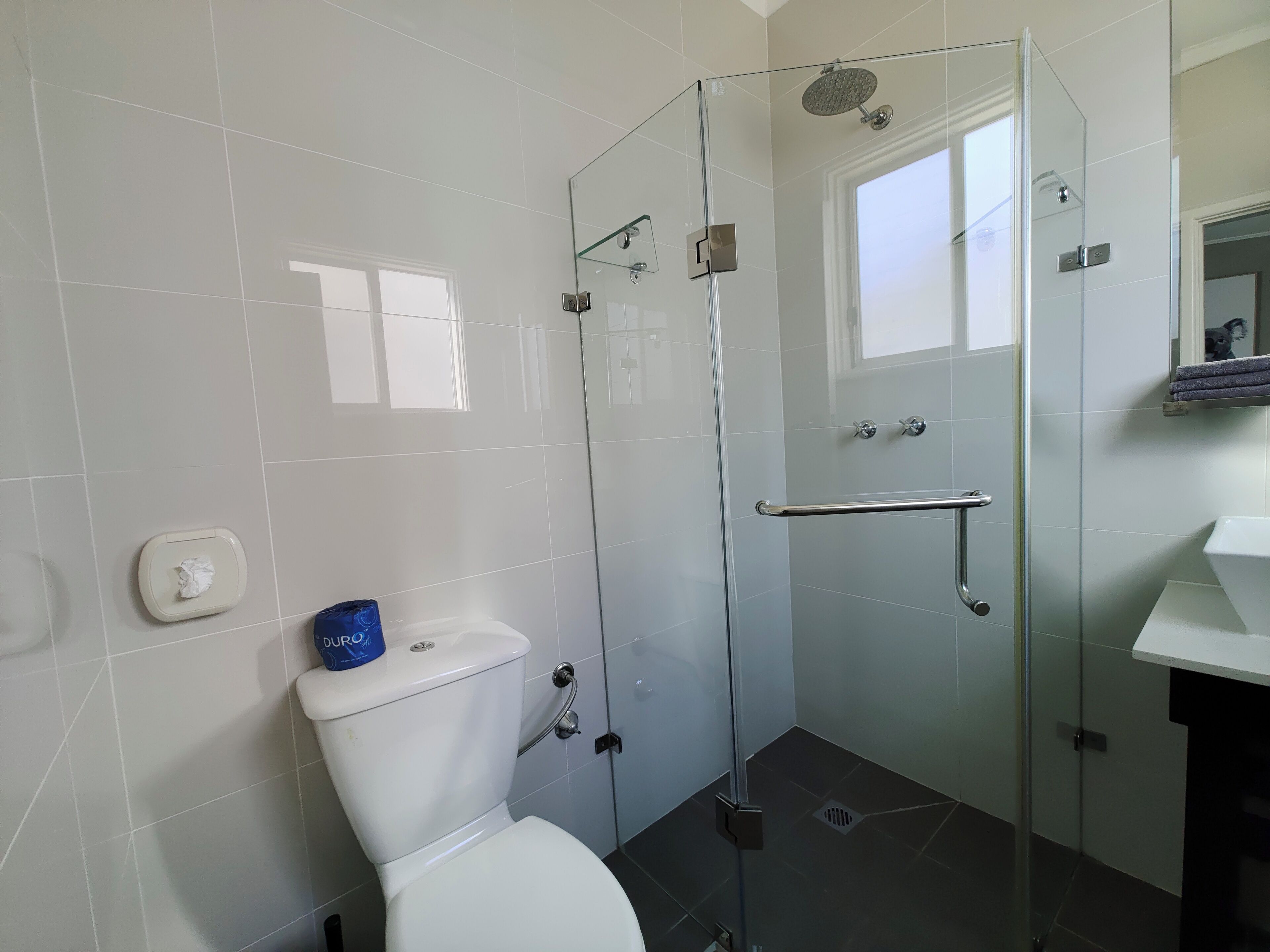 A modern bathroom with a glass-enclosed shower, a white toilet, and a visible window.