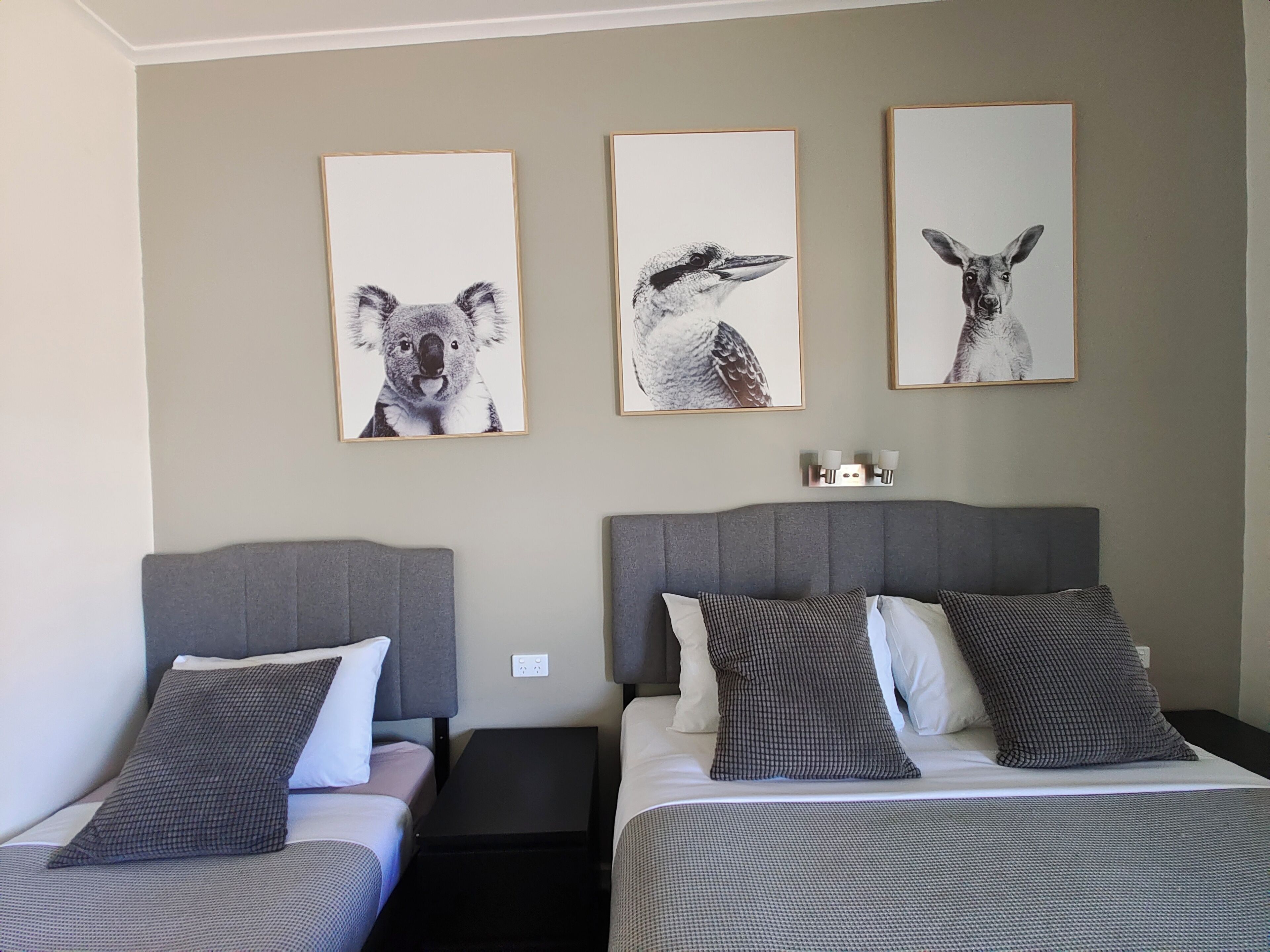 A hotel room with two beds, grey headboards, and three framed animal portraits on the wall.