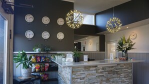 Zona de recepción con mostrador de piedra, varios relojes que marcan diferentes husos horarios, y lámparas colgantes de forma esférica.