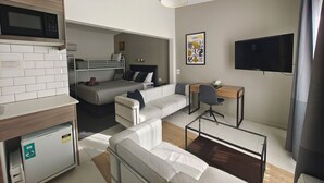 Un espacio habitable moderno y compacto con kitchenette, un sofá, un escritorio y un televisor.