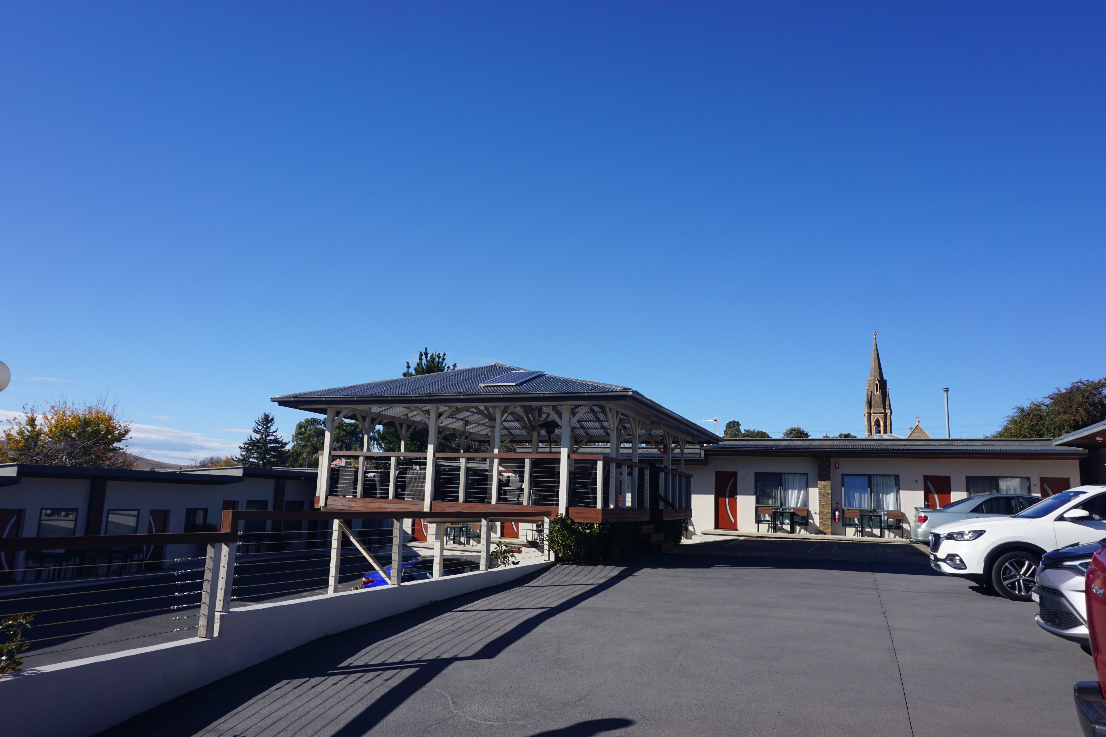 A building with a covered outdoor area, a parking lot, and a church in the background.