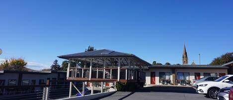 A building with a covered outdoor area, a parking lot, and a church in the background.