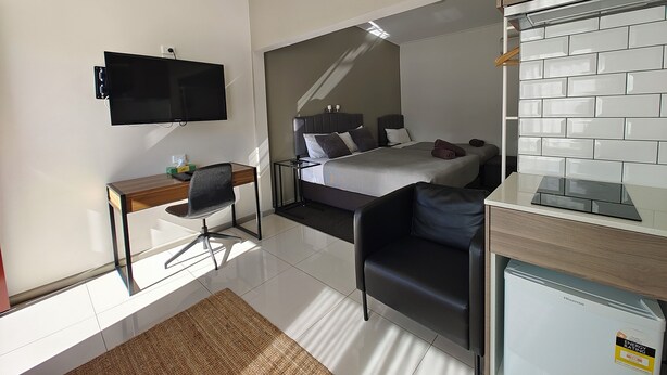 Una habitación de hotel moderna con cama, escritorio, silla, televisor y refrigerador.